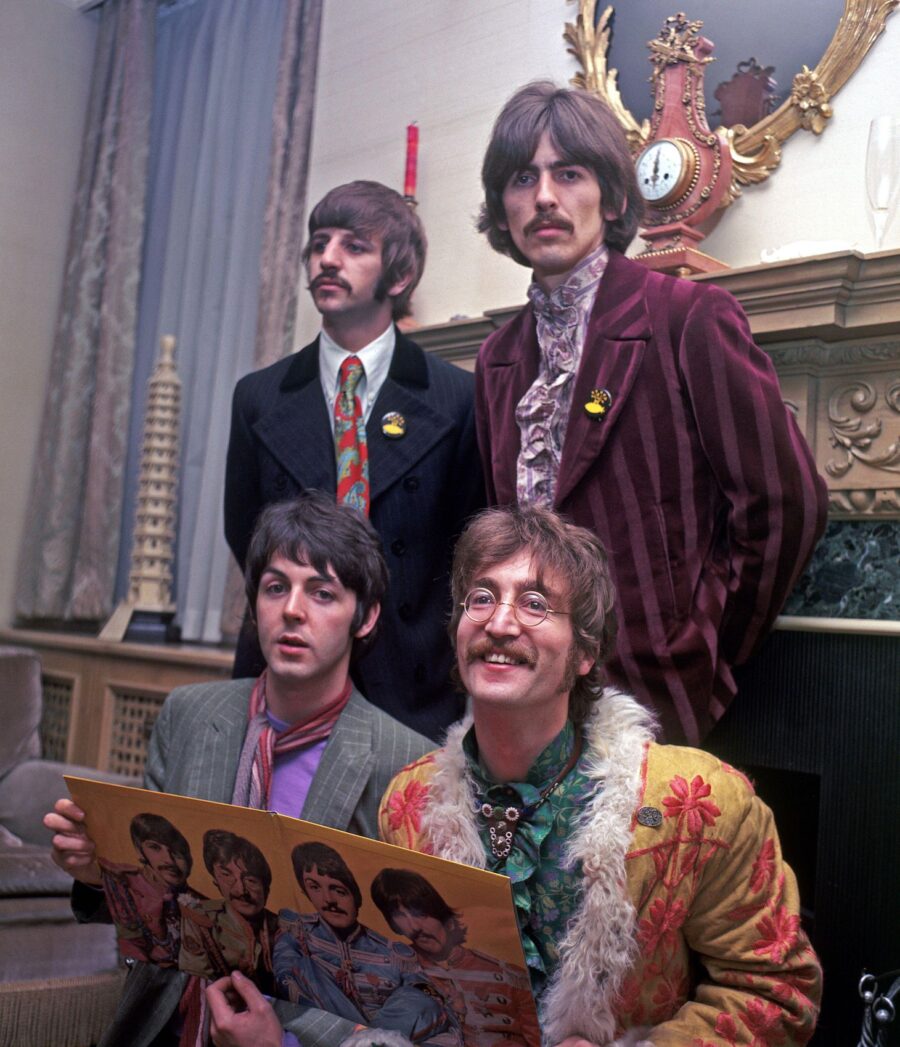 The Beatles pose in colorful outfits, holding their "Sgt. Pepper's Lonely Hearts Club Band" album. A vintage setting enhances their iconic style.