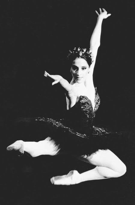 Ballet dancer in a dramatic pose, showcasing elegance and strength, dressed in a black tutu with a floral tiara against a dark background.