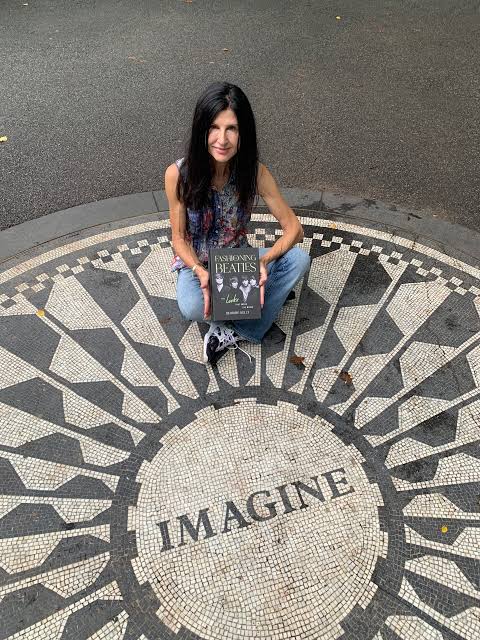 A woman sits on a mosaic in Central Park, holding a book titled "Fashioning the Beatles" with the word "IMAGINE" prominently displayed beneath her.